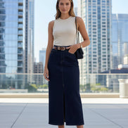Person wearing a navy denim skirt with a white top and brown sandals indoors.