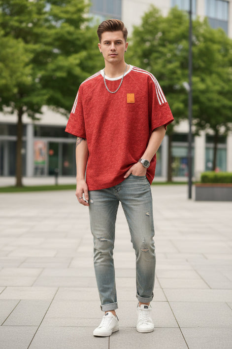 Red t-shirt with white stripes on sleeves and a patch, worn by a person against a gray background.