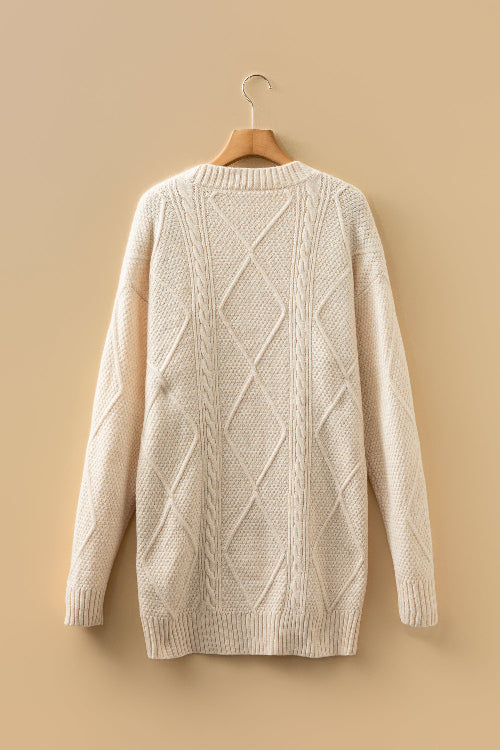 Beige cable knit sweater on a wooden hanger against a beige background