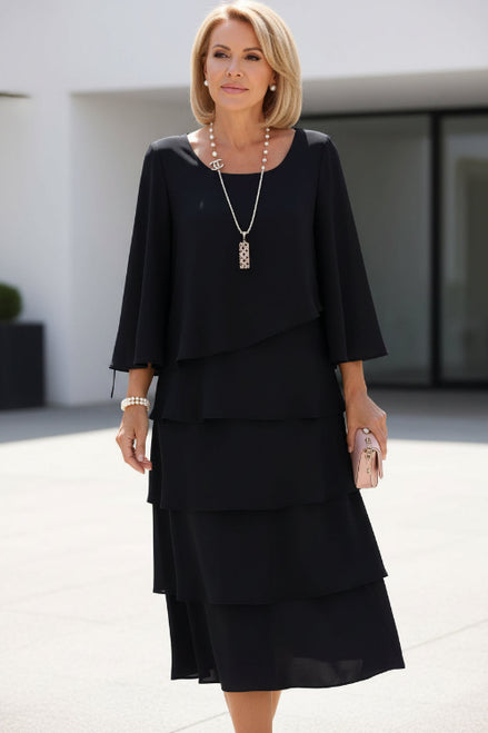 Woman wearing a black layered dress holding a pink clutch against a white background