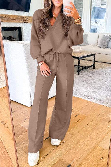 A woman takes a mirror selfie wearing a matching brown lounge set consisting of a long-sleeve V-neck top and wide-leg drawstring pants, 