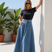 Person wearing a black t-shirt and blue denim skirt against a white wall.