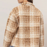 Person wearing a plaid shirt with a neutral color palette on a plain background