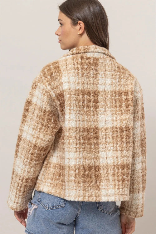 Person wearing a plaid shirt with a neutral color palette on a plain background