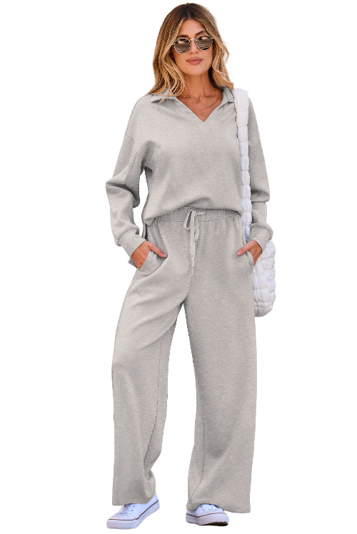 A woman modeling a light gray two-piece loungewear set consisting of a long-sleeve collared top and matching wide-leg sweatpants, 