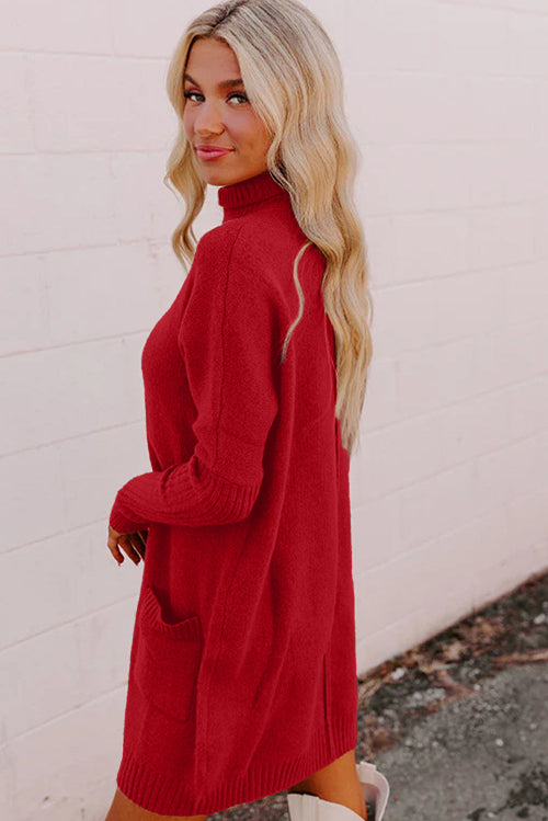 Woman wearing a red sweater dress against a light pink wall.
