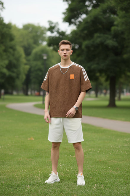 Brown t-shirt with white stripes on sleeves and a small patch on chest, worn by a person.