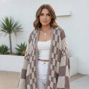 Woman wearing a checkered crochet cardigan over a white top and pants, standing indoors.
