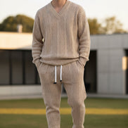 A person modeling a matching beige cable-knit sweater and jogger pants set with white drawstrings, 