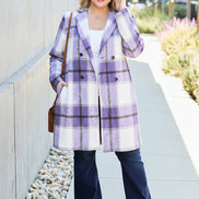 Woman wearing a purple plaid coat with a white shirt and blue pants, standing on a sidewalk.