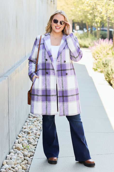 Woman wearing a purple plaid coat with a white shirt and blue pants, standing on a sidewalk.