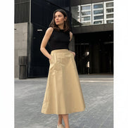 Woman wearing a black top and beige skirt standing on a paved street.
