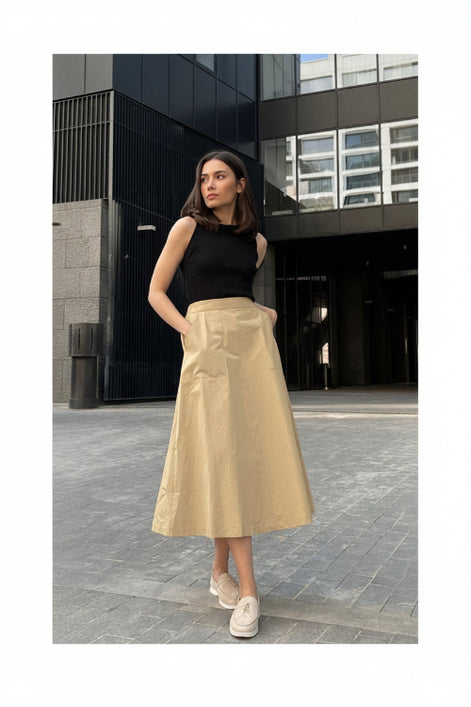 Woman wearing a black top and beige skirt standing on a paved street.