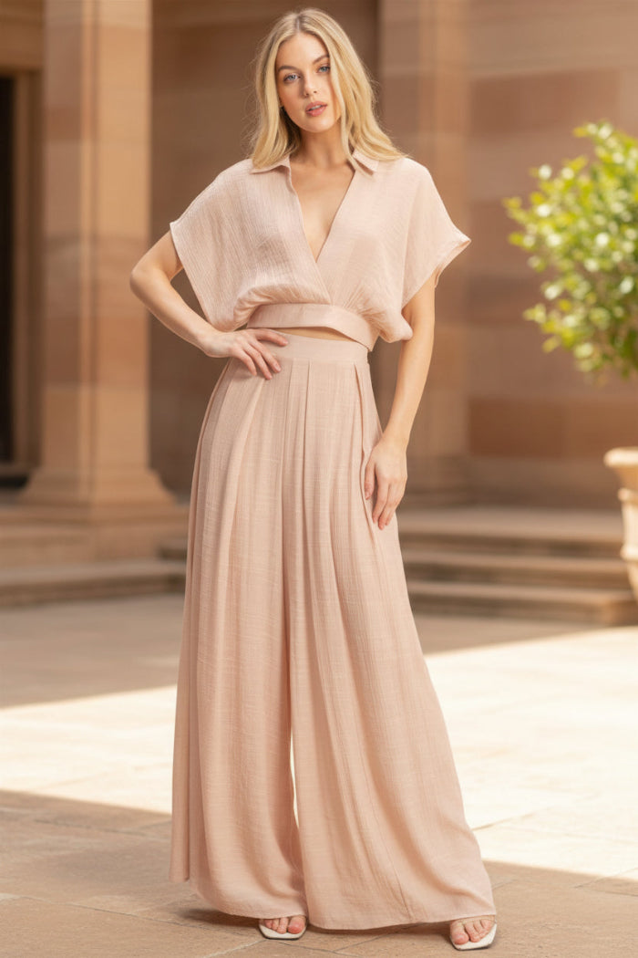 Woman wearing a light pink outfit with a top and long skirt on a plain background