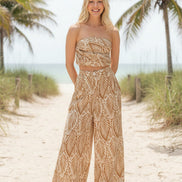 Woman wearing a matching strapless top and wide-leg pants with a leaf pattern on a plain background