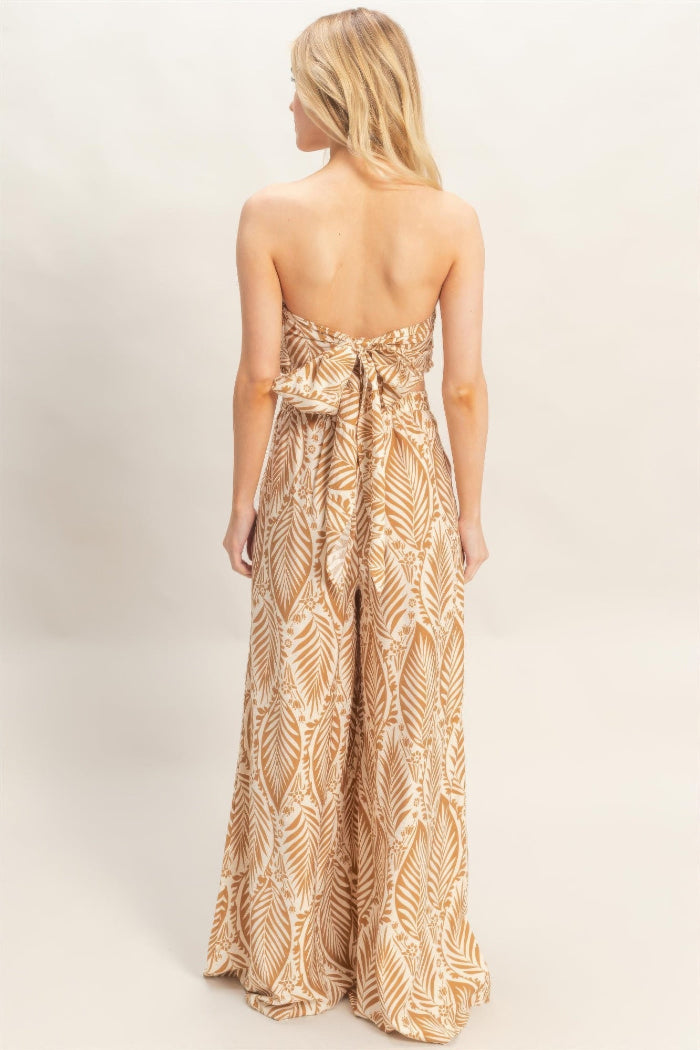 Woman wearing a strapless, long, patterned dress on a plain background