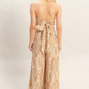 Woman wearing a strapless, long, patterned dress on a plain background