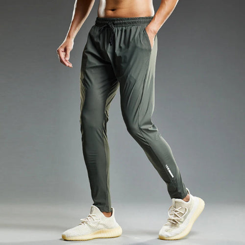 Person wearing dark gray athletic pants and white sneakers on a gray background