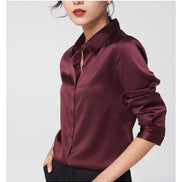 Maroon satin button-front shirt with rolled sleeves, worn by a model at an angle against a light gray background