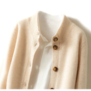 A close-up of a cream-colored knit cardigan with brown buttons, layered over a white collared shirt against a plain white background.