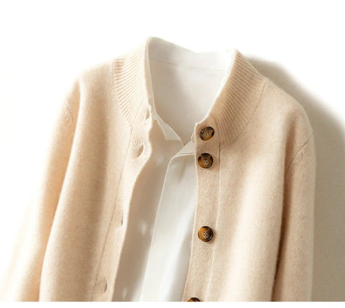 A close-up of a cream-colored knit cardigan with brown buttons, layered over a white collared shirt against a plain white background.