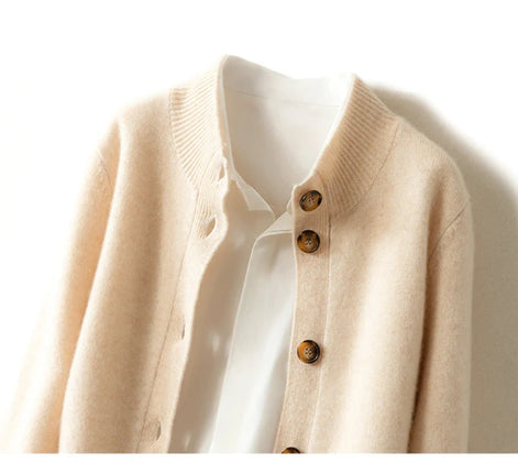 A close-up of a cream-colored knit cardigan with brown buttons, layered over a white collared shirt against a plain white background.
