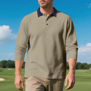 Front view of men's taupe long sleeve polo shirt with a contrasting navy collar and three-button placket, modeled on a golf course with sleeves pushed up and khaki trousers