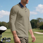 Angled front view of men's taupe long sleeve polo shirt with a contrasting navy collar and three-button placket, modeled beside golf clubs on a golf course