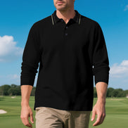 Front view of men's black long sleeve polo shirt with fine contrasting collar stripes and a button placket, modeled on a golf course with sleeves pushed up and khaki trousers
