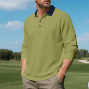 Men's army green long sleeve polo shirt with a contrasting navy collar and three-button placket, modeled outdoors with sleeves pushed up and taupe trousers