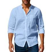 Men's light blue linen blend stand collar shirt with a button front, chest pocket, and rolled sleeves, worn with dark blue jeans