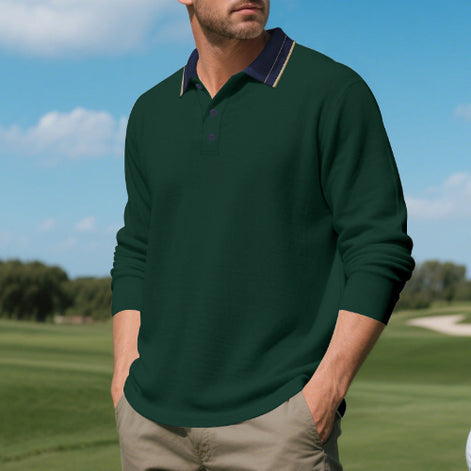 Men's dark green long sleeve polo shirt with a contrasting navy collar and three-button placket, modeled outdoors with sleeves pushed up and taupe trousers