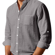 Angled front view of men's gray linen blend stand collar shirt with a button front, chest pocket, and rolled sleeves, tucked into jeans with a brown belt