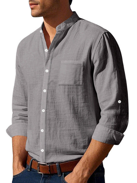 Angled front view of men's gray linen blend stand collar shirt with a button front, chest pocket, and rolled sleeves, tucked into jeans with a brown belt