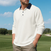 Men's white long sleeve polo shirt with a contrasting navy collar and three-button placket, modeled outdoors with sleeves pushed up and taupe trousers