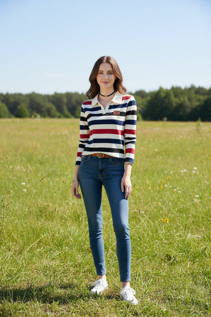 A woman wearing a long-sleeve collared knit top with horizontal stripes in cream, navy blue, black, and red. The top has a small brown patch on the left chest.