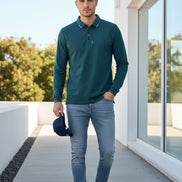 Teal polo shirt with collar and brand logo held by a hand, with blurred background