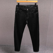 Black slim-fit jeans hanging on a wooden hanger against a textured gray wall.
