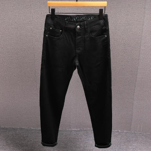 Black slim-fit jeans hanging on a wooden hanger against a textured gray wall.
