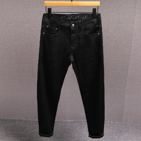 Black slim-fit jeans hanging on a wooden hanger against a textured gray wall.