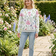A woman wearing a white crewneck sweatshirt with a colorful watercolor floral print featuring pink, purple, and green flowers and leaves.