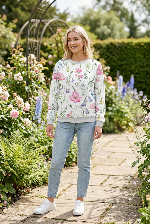 A woman wearing a white crewneck sweatshirt with a colorful watercolor floral print featuring pink, purple, and green flowers and leaves.