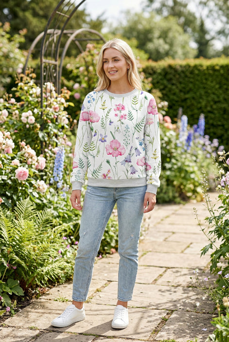 A woman wearing a white crewneck sweatshirt with a colorful watercolor floral print featuring pink, purple, and green flowers and leaves.