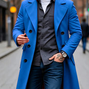A man wearing a bright blue double-breasted overcoat over a dark gray button-up shirt, white t-shirt, and blue jeans, walking on a blurred city street.