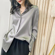 Gray satin button-down shirt worn by a model standing against curtains.