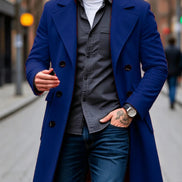 A man wearing a vibrant royal blue double-breasted overcoat over a dark gray button-down shirt, white t-shirt, and blue jeans, standing on a city street.