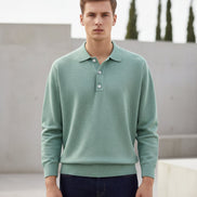Person wearing a light green sweater over a collared shirt with dark jeans on a plain background