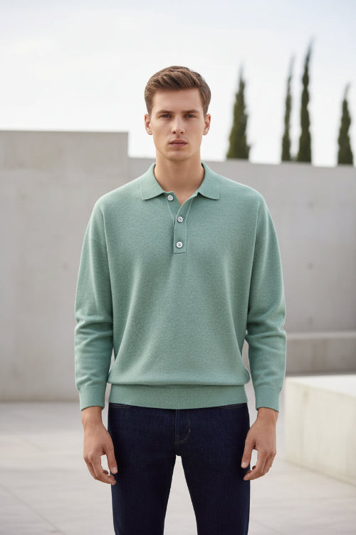 Person wearing a light green sweater over a collared shirt with dark jeans on a plain background