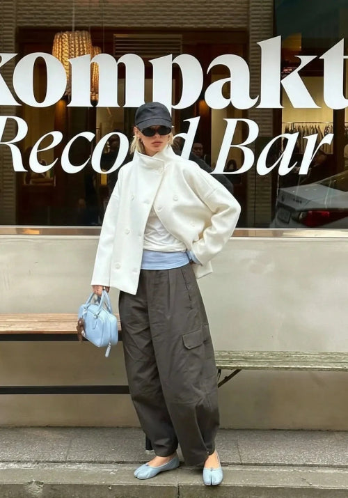 Woman wearing an off-white short coat partly open with gray cargo trousers