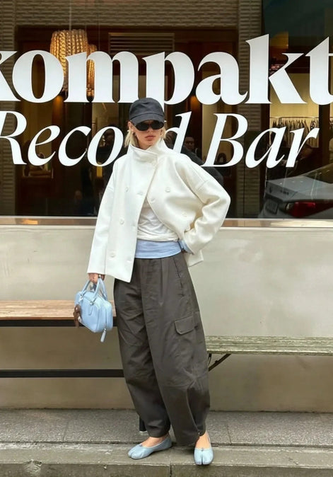 Woman wearing an off-white short coat partly open with gray cargo trousers